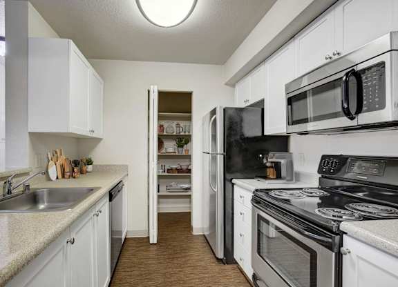 Galley kitchen with white cabinetry, dark appliances, and generous counter space.