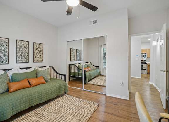 A bedroom with a green couch and a mirrored closet door.