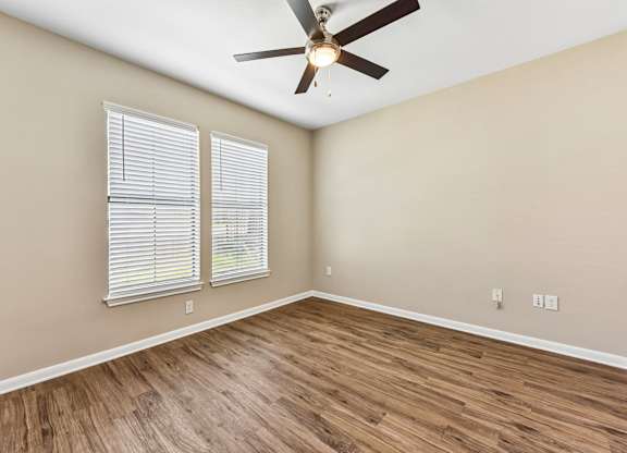 A room with a ceiling fan and two windows with blinds.