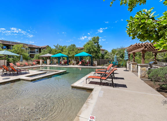 a swimming pool with chairs and umbrellas in front of a house at Lakeline East Apartments, Cedar Park, TX