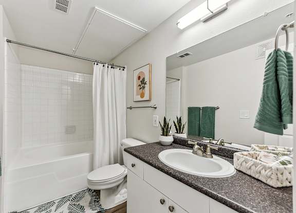 A bathroom with a white toilet, a white sink, and a white bathtub with a white shower curtain. at Stone Oak @ Parmer, Austin, Texas