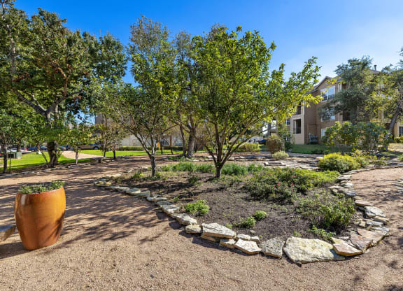a garden with trees and rocks and a building in the background at Sonterra Apartment Homes, Austin, TX