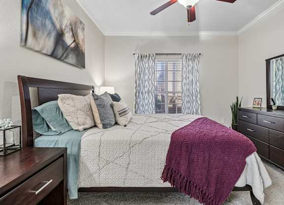 A bedroom with a bed, a ceiling fan, and a painting on the wall.