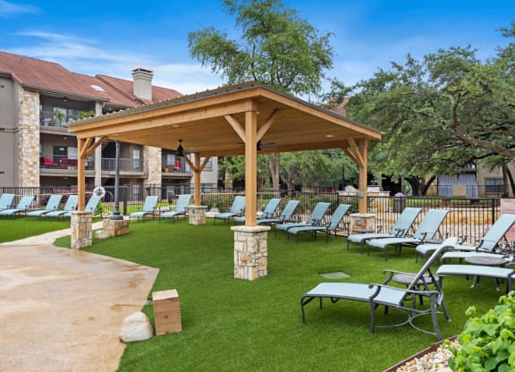 A pavilion with chaise lounge chairs on a grassy area with trees in the background at Waters Edge Apartment Homes, Texas, 78626