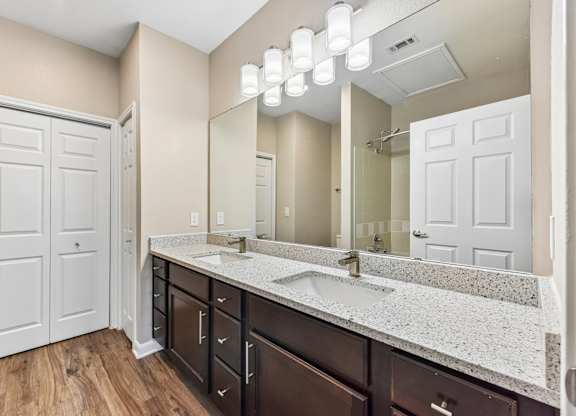 A bathroom with a white door, brown cabinets, and a marble countertop.
