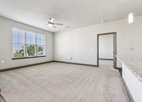 A spacious room with a carpeted floor, a ceiling fan, and a large window with blinds.at North Creek, Hutto, Texas