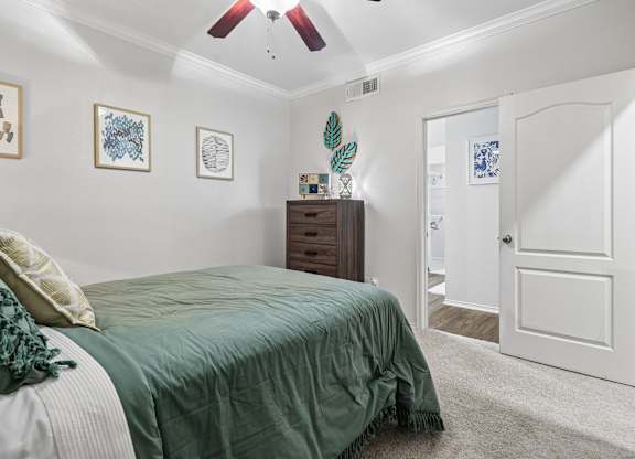 A bedroom with a bed, a ceiling fan, and a dresser.
