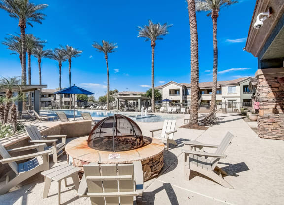a fire pit with chairs around it near a pool with palm trees  at Adiamo Palm Valley, Goodyear, AZ
