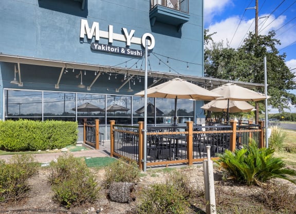 an outdoor patio with umbrellas and tables in front of a blue building at Artisan Apartments & Shops, Texas