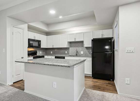 A kitchen with a black refrigerator and white cabinets.