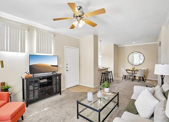 A living room with a television, a sofa, a chair, a table, and a ceiling fan.