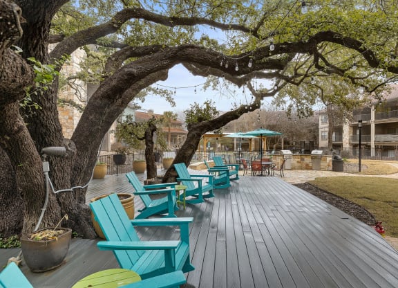A group of blue chairs sitting on a wooden deck under a tree at Waters Edge Apartment Homes, Georgetown