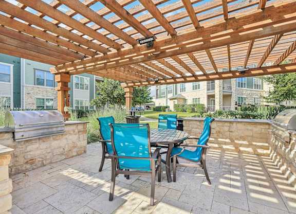 A wooden pergola with a table and chairs is set up on a patio. North Creek, Hutto, TX