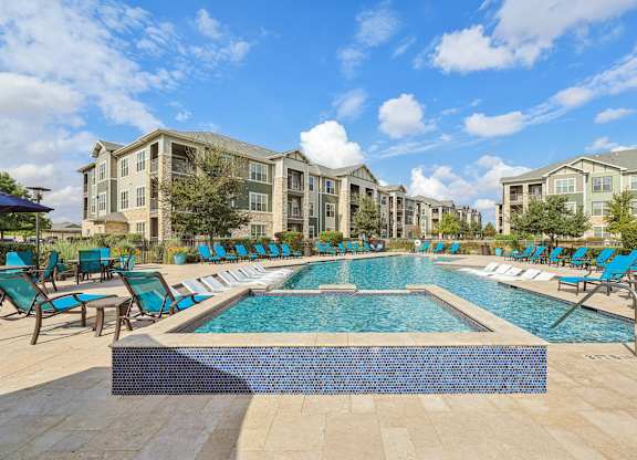 A large swimming pool surrounded by lounge chairs in front of apartment buildings. at North Creek, Hutto