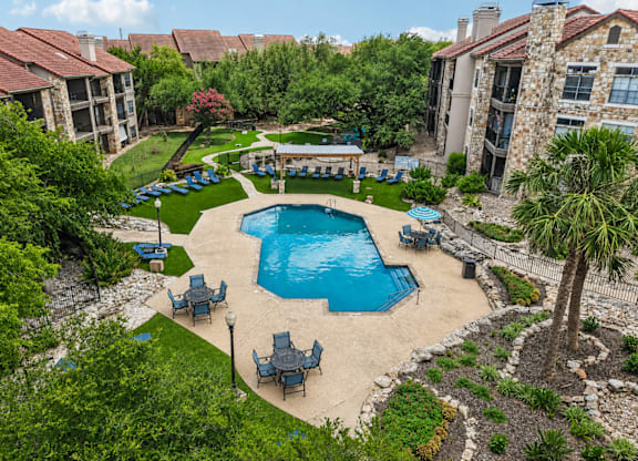 A swimming pool surrounded by lawn chairs and trees.