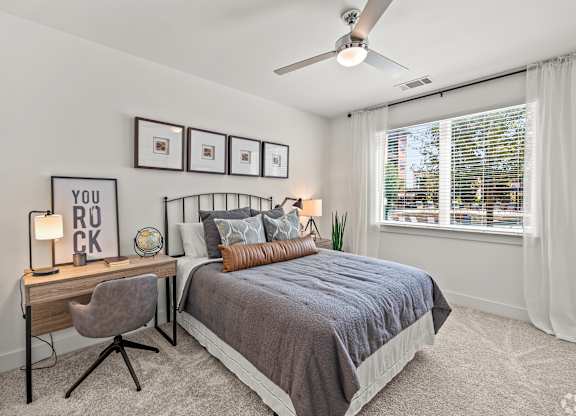 A bedroom with a bed, desk, chair, and pictures on the wall.