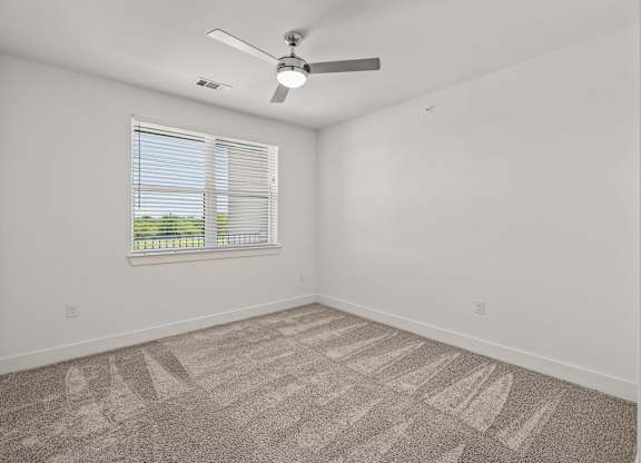A room with a fan, carpet, and a window.