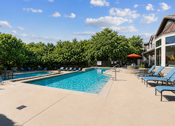 A large outdoor swimming pool surrounded by trees and lounge chairs.