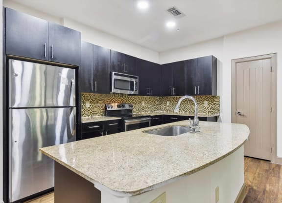 a kitchen with black cabinets and a granite counter top and a stainless steel refrigerator at Lakeline East Apartments, Cedar Park