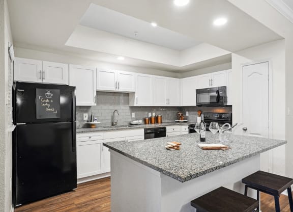 a kitchen with a granite counter top and a black refrigerator at La Ventura Apartments, Plano, Texas