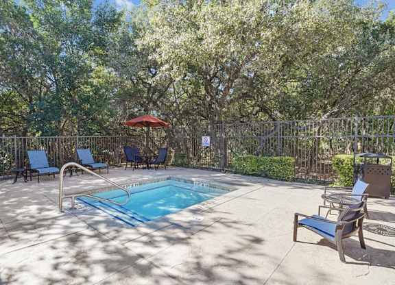 a pool with chairs and an umbrella in a backyard with trees