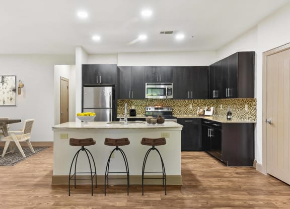a kitchen with black cabinets and a counter with three stools at Lakeline East Apartments, Cedar Park, TX