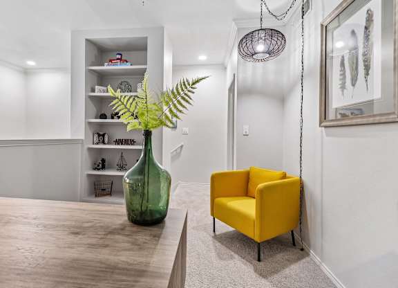 A green vase with a fern sits on a wooden table next to a yellow chair.