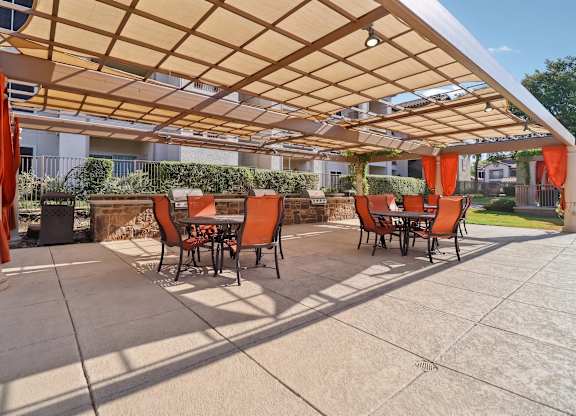A patio with orange chairs and a wooden pergola.