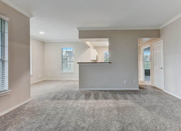 an empty living room with carpet and a kitchen