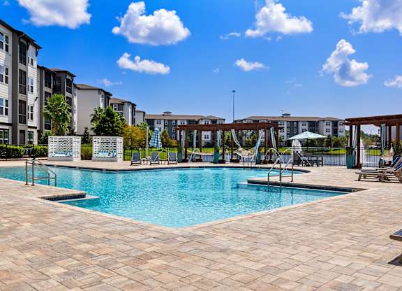 A large swimming pool surrounded by a tiled patio and lounge chairs.