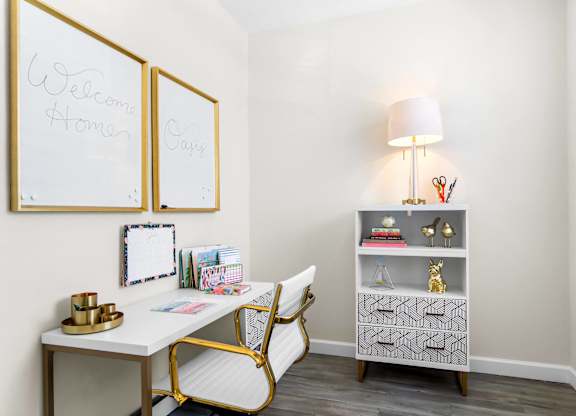 A white desk with a gold chair and a lamp on a grey shelf.
