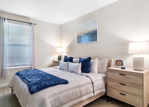 A bedroom with a bed, nightstand, and a painting on the wall.