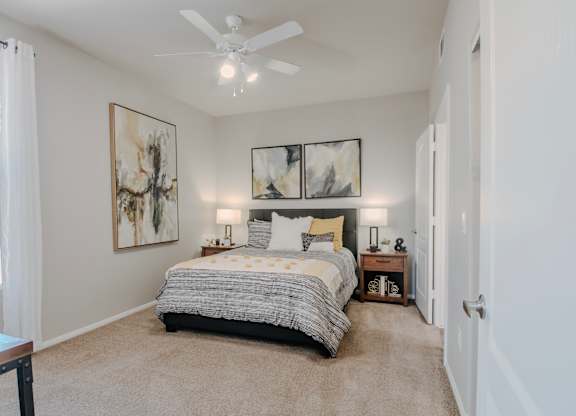 A bedroom with a bed, two lamps, and two framed pictures on the wall.