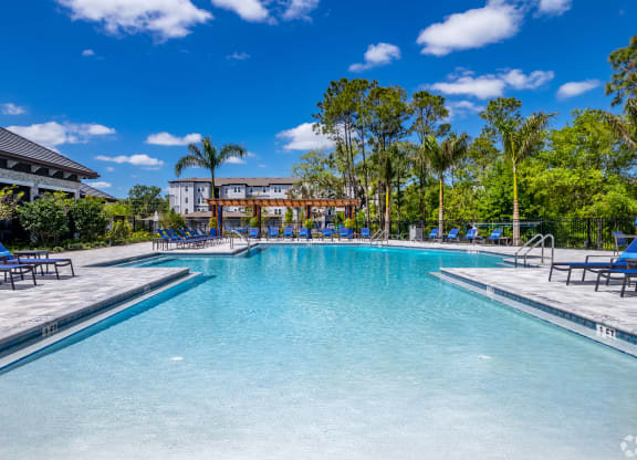 a large swimming pool with chaise lounge chairs and a building in the background at The Oasis at Manatee River, Bradenton, FL, 34211