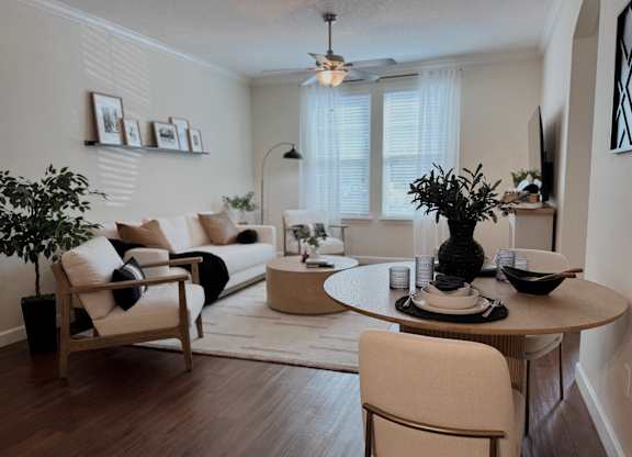 A living room with a white couch, a wooden chair, a round table with a vase on it, and a potted plant.