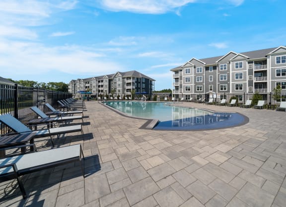 a swimming pool with lounge chairs around it in front of an apartment building at The Oasis at Plymouth, Plymouth, MA, 02360