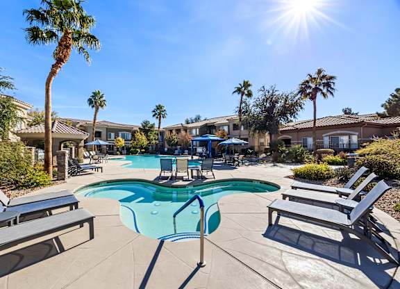 A sunny day at the pool with lounge chairs and palm trees.