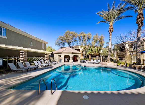 A swimming pool surrounded by sun loungers and palm trees.