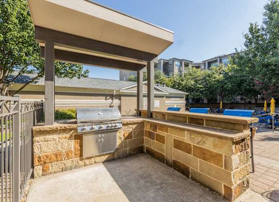 Outdoor grill station with tall table and stools close to the pool at Encore at Buckingham apartments in Richardson, TX
