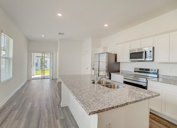 Oak floor plan kitchen with granite counters, a kitchen island, and stainless steel appliances at Beacon at Clinton Corners in Dade City, FL