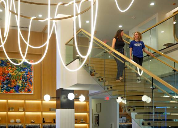 Two women are walking up a glass staircase.