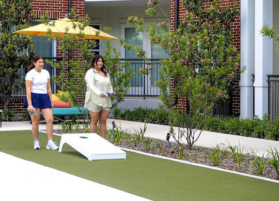 Two women playing cornhole in a garden.