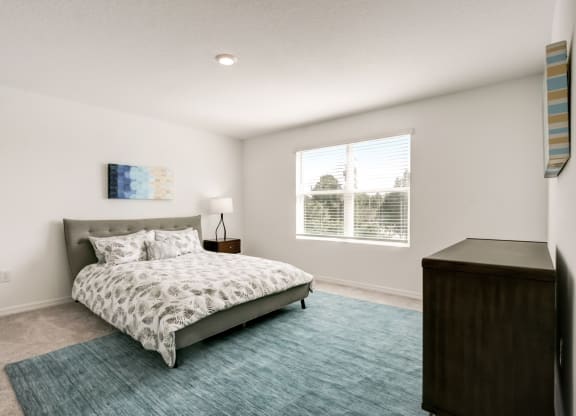 Furnished master bedroom with a bed, blue rug, dresser, and a window at Beacon at Arbours in Ruskin, FL