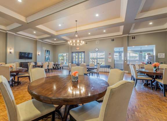 Grand ballroom with several tables and seating, a tv, and kitchen with a coffee maker machine at Encore at Buckingham apartments in Richardson, TX