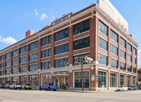 Side view of the Adam Hats Lofts building on a clear sunny day with cars parked on front | Adam Hats Lofts from Deep Ellum Lofts in Dallas, TX