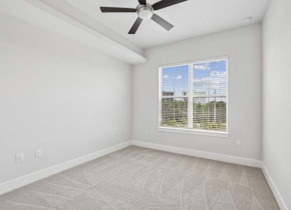 A carpeted bedroom from the C1 floorplan with a ceiling fan and a window with blinds at Alastair at Aria Village Apartments in Sandy Springs, GA