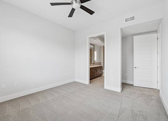 A carpeted bedroom from the C1 floorplan with a ceiling fan and connected bathroom at Alastair at Aria Village Apartments in Sandy Springs, GA