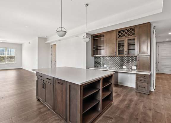 A modern kitchen from the C1 floorplan with a white countertop and island, brick backsplash, and wooden cabinets at Alastair at Aria Village Apartments in Sandy Springs, GA