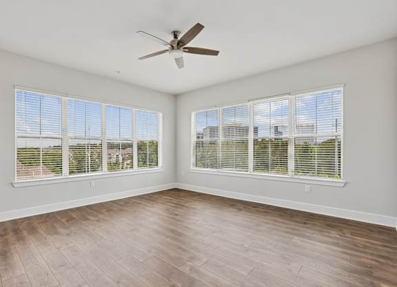 A living room from the C1 floorplan with a ceiling fan, wood floors, and large windows at Alastair at Aria Village Apartments in Sandy Springs, GA
