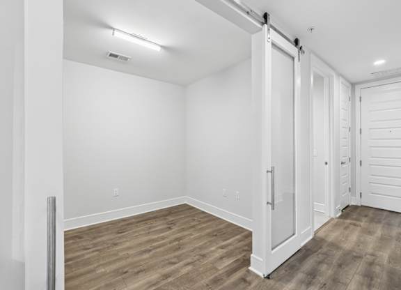 A study from the C1 floorplan with white walls, wooden flooring, and sliding barn doors at Alastair at Aria Village Apartments in Sandy Springs, GA